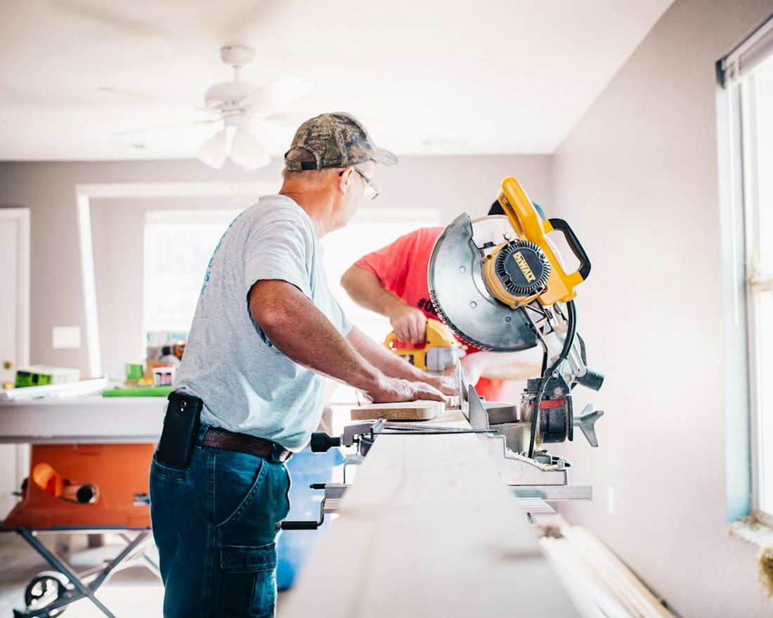 Two tradespeople cutting trim with a mitre saw in a bright room under renovation