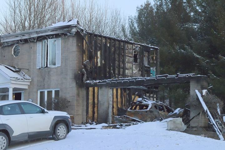 A fire-damaged house in winter, with the garage burned down to its framing
